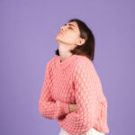 Giovane bruna in maglione rosa isolata sulla parete viola